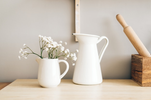 Foto jarra blanca y flores en un jarrón sobre una mesa de madera en la cocina