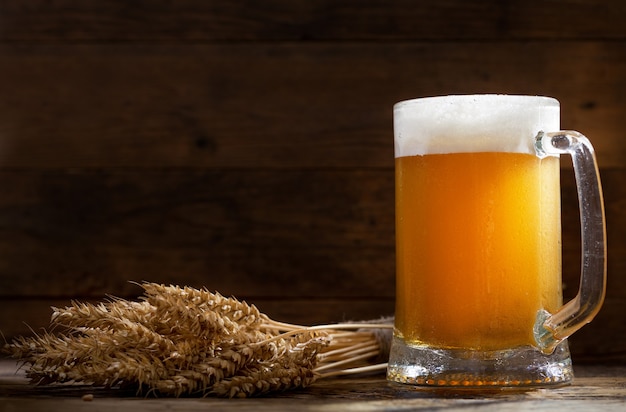 Jarra de cerveza con espigas de trigo en la mesa de madera