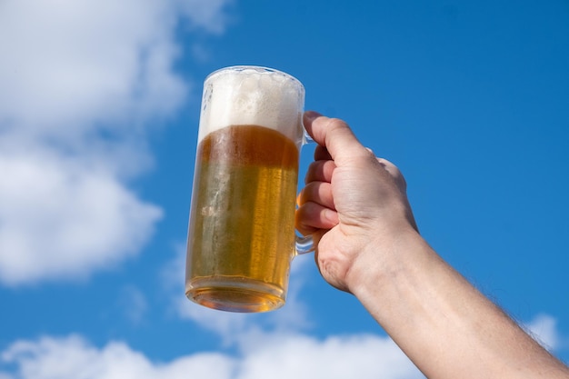 Foto una jarra de cerveza fría contra el cielo azul. un hombre sostiene una jarra de cerveza.