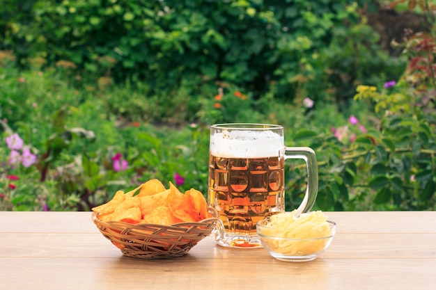 Jarra de cerveza en la mesa de madera con papas fritas en canasta de mimbre y calamares secos en un tazón