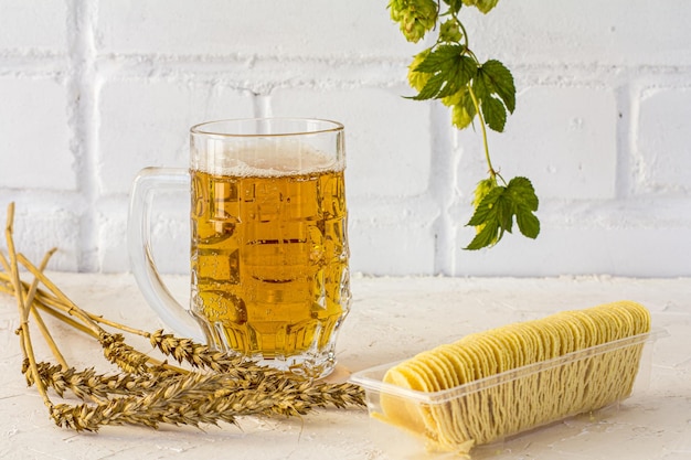 Jarra de cerveza con papas fritas, espigas de cebada y una rama de lúpulo sobre el fondo blanco.