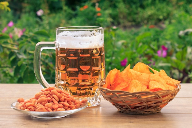 Jarra de cerveza de vidrio en la mesa de madera con papas fritas en una canasta de mimbre maní en un plato en el escritorio