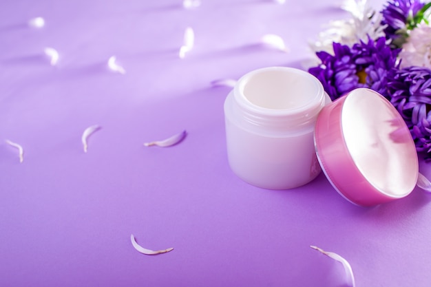 Jarra com creme rodeado de flores sobre fundo roxo