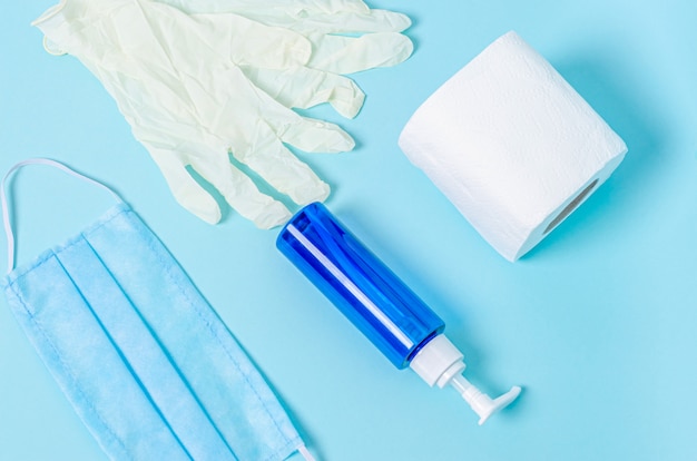 Jarra com sabonete líquido, papel higiênico, máscara médica protetora, luvas de borracha branca sobre uma superfície azul