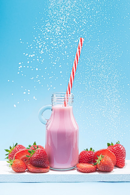 Jarra de Milk Shake de morango com palha, morangos e açúcar voador sobre fundo azul