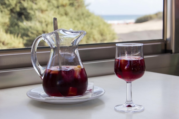 Jarra de sangria e copo na mesa branca com vista para a praia em um dia ensolarado. bebida alcoólica refrescante