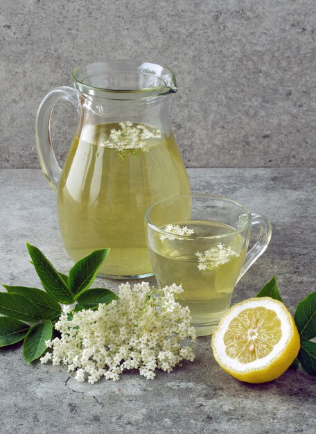 Jarra e um copo com uma bebida de flores de sabugueiro com uma rodela de limão.