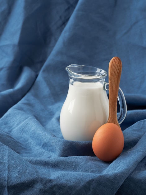 Foto jarra con leche, una cuchara de madera y un huevo de gallina.