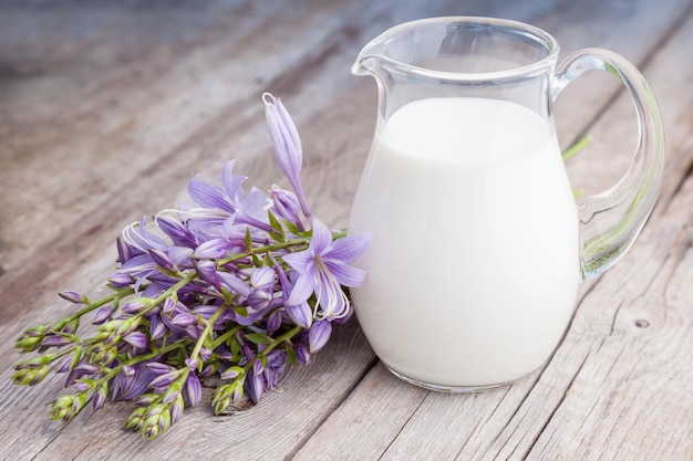 Jarra de leche fresca y ramo de flores de campanillas en tablero rústico de madera