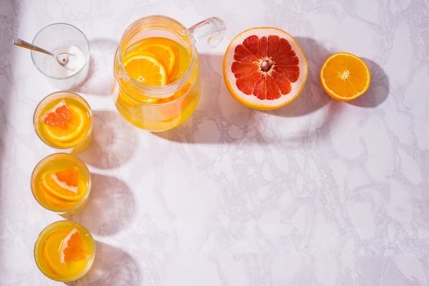 Jarra de limonada con naranjas, limones y pomelos en la mesa. vasos de limonada disparó desde la vista aérea sobre la mesa blanca.