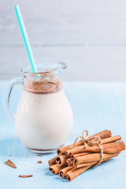 Jarra de vaso de leche con canela y tubo de cóctel sobre fondo de madera azul