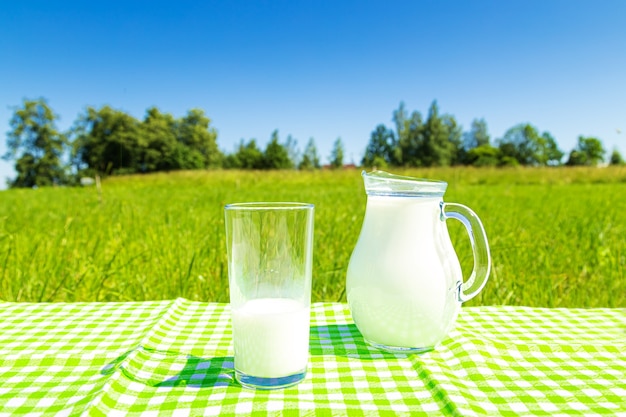 Jarra y vaso de leche sobre un fondo de campo verde y cielo azul. Alimentación saludable.