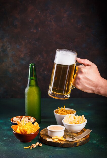 Jarra de vidrio con cerveza con espuma y gotas de agua y bocadillos en verde oscuro