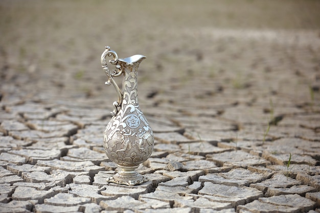 Jarro de água antigo de prata em um deserto seco.