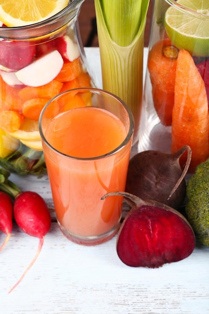 Foto jarro de legumes cortados e um copo de suco de cenoura fresca com legumes em uma mesa de madeira