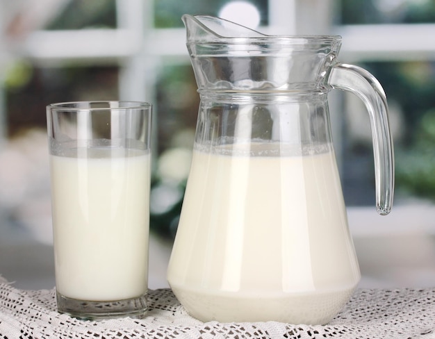 Jarro y vaso de leche en una mesa de madera en el fondo de la ventana