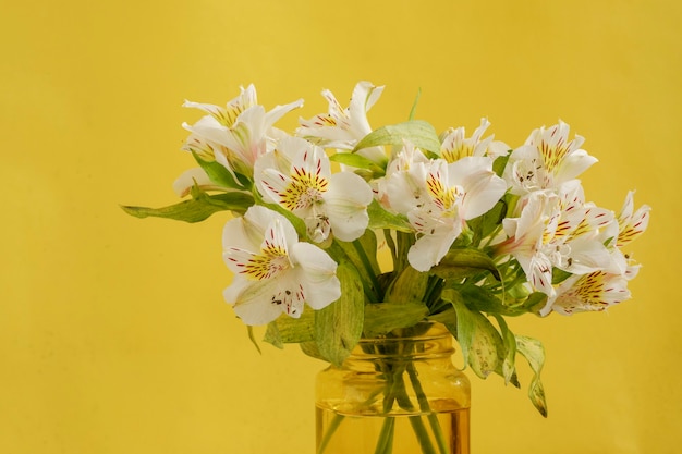 Jarrón amarillo con ramo de flores blancas sobre una mesa de mármol y fondo amarillo