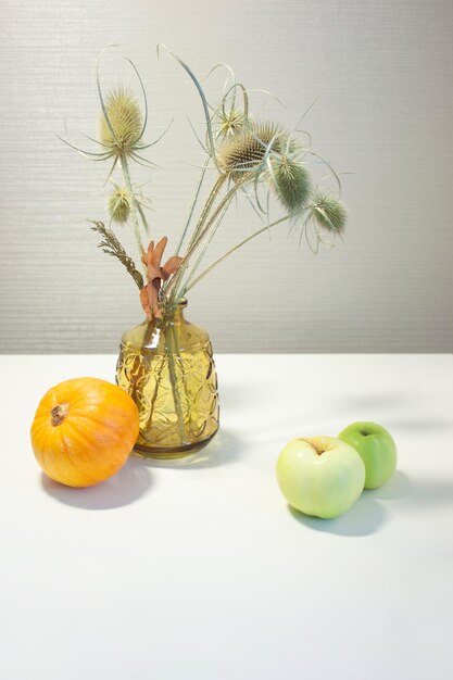 Jarrón de cristal de calabaza con Dipsacus y manzanas verdes Cosecha del Día de Acción de Gracias de otoño