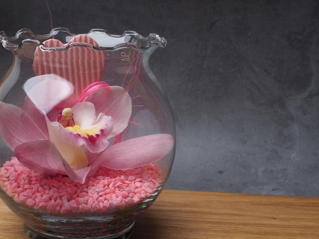 Un jarrón de cristal con piedras rosas y una flor.