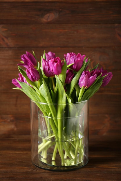 Jarrón de cristal con ramo de hermosos tulipanes sobre fondo de madera