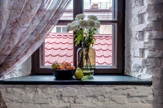 Jarrón con flores en el alféizar de la ventana en estilo antiguo con frutas o velas