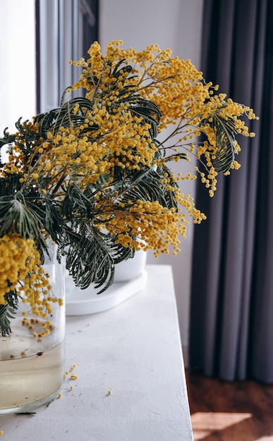 Un jarrón de flores amarillas con bayas amarillas sobre una mesa blanca.