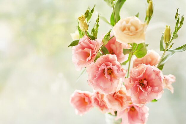 Jarrón con flores de eustoma sobre una mesa contra una ventana