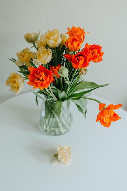 Un jarrón de flores naranjas y amarillas sobre una mesa blanca