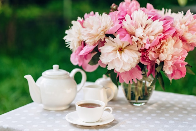 Un jarrón de flores de peonías cerca de una taza de café.