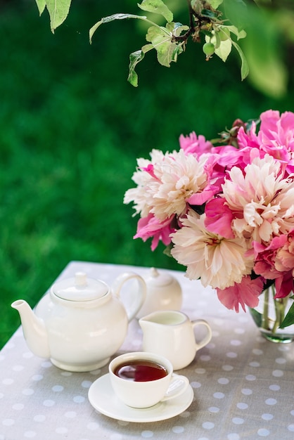 Un jarrón de flores de peonías cerca de una taza de té