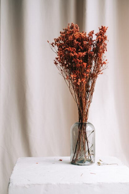 Jarrón con flores secas rojas sobre una mesa blanca sobre tela satinada