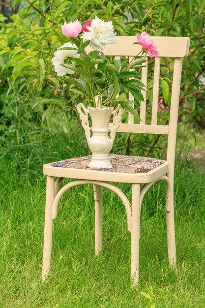 Jarrón de flores con una silla blanca de estilo rústico en el jardín.