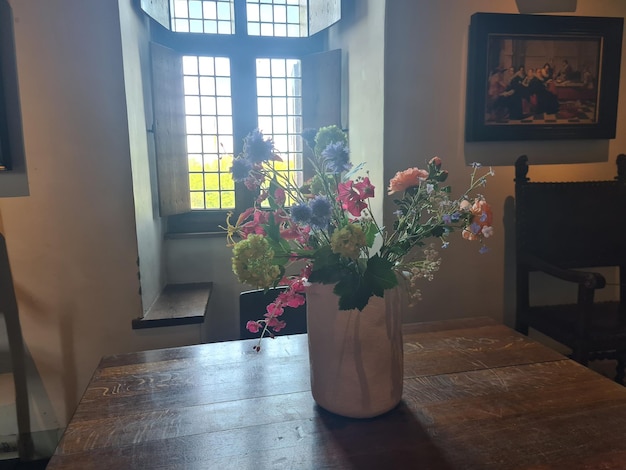 Un jarrón con flores sobre una mesa y una ventana detrás
