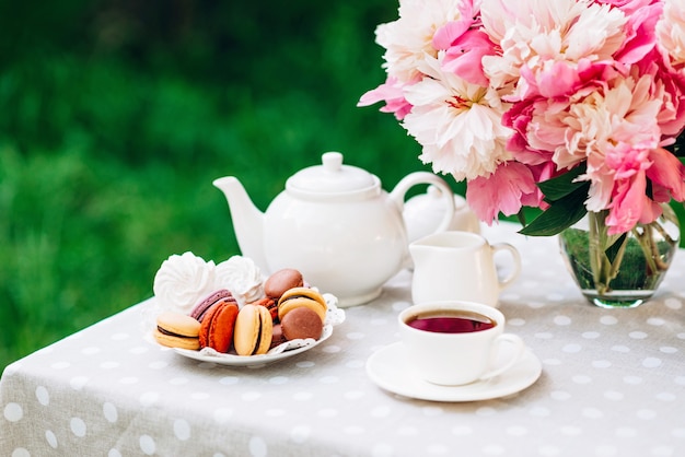 Un jarrón con peonías, una tetera y una taza de té sobre la mesa