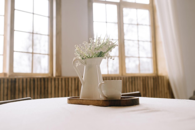 Jarrón con pequeñas flores blancas sobre la mesa sobre un fondo de grandes ventanales con espacio para texto