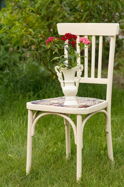 Jarrón de porcelana con ramo de flores de clavel en una silla blanca de estilo rústico en el jardín de verano con fondo natural.