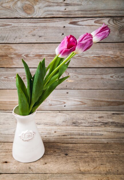 Jarrón con tulipanes naturales sobre una mesa de madera