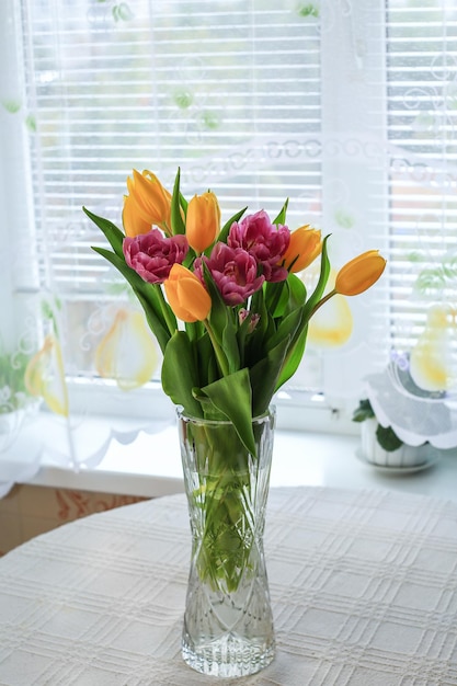Un jarrón de tulipanes se sienta en una mesa redonda frente a una ventana