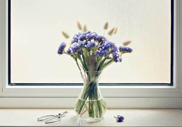 Jarrón de vidrio con flores azules en el alféizar de la ventana.