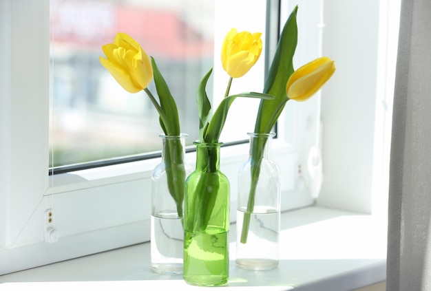 Jarrones de cristal con hermosos tulipanes en el alféizar de la ventana