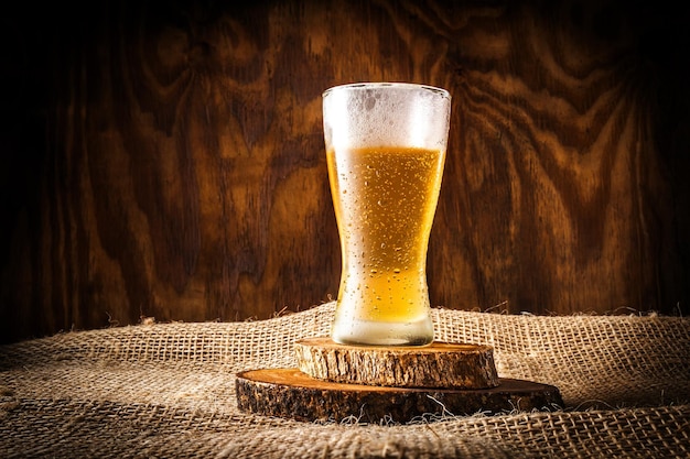 Jato de cerveja derramando em um copo de cristal em um fundo texturizado de madeira azul
