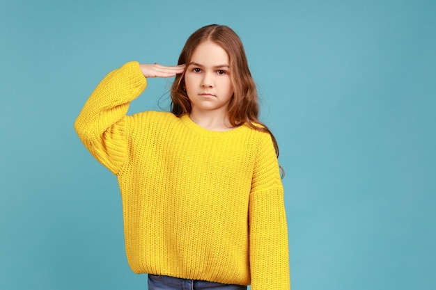 Jawohl. Porträt eines kleinen Mädchens, das respektvoll in die Kamera blickt, patriotisches Kind, das einen gelben Pullover im lässigen Stil trägt. Studioaufnahme im Innenbereich isoliert auf blauem Hintergrund.