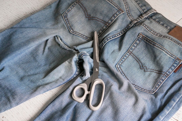 Jeans velhos e rasgados estão espalhados sobre a mesa, prontos para serem consertados. As mãos da mulher estão segurando jeans. O conceito de consertar roupas, reciclar, passatempos domésticos e trabalhar remotamente.