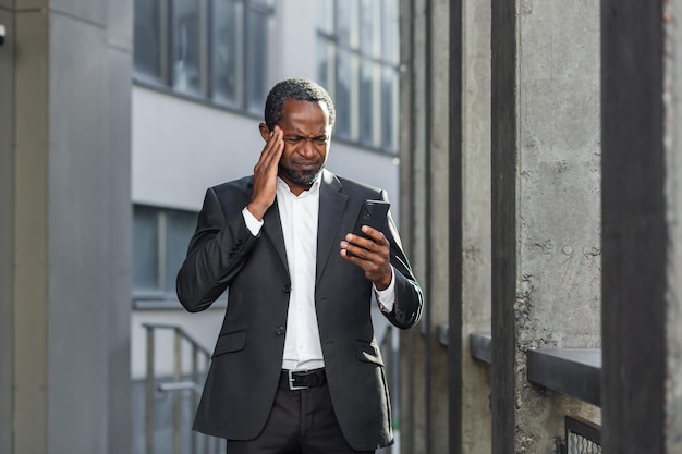 Jefe afroamericano fuera del edificio de oficinas con el teléfono en las manos leyendo malas noticias en línea hombre