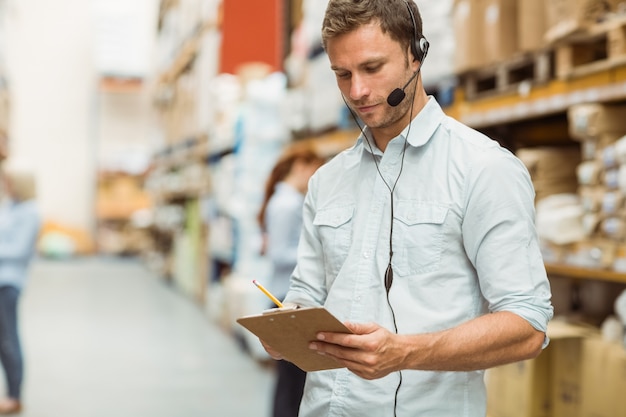 Jefe de almacén usando auriculares escribiendo en portapapeles