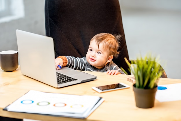Jefe de bebé que trabaja con el portátil sentado en la silla en la oficina