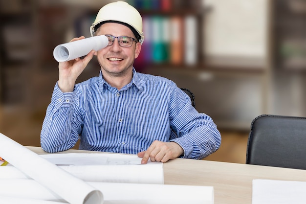 Foto el jefe en el casco de construcción en la mesa con la documentación del proyecto mira un dibujo enrollado. finalización exitosa del proyecto. constructor, ingeniero, jefe, capataz.