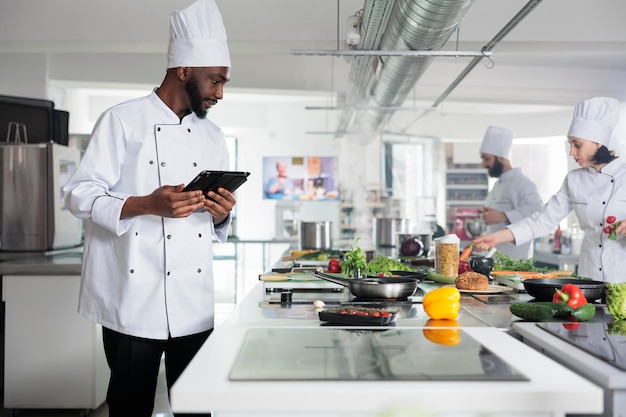 Jefe de cocina con tabletas con ideas de guarnición para una comida de cocina gourmet. Trabajador de la industria alimentaria con dispositivo de pantalla táctil portátil que prepara ingredientes para el servicio de cena en el restaurante.