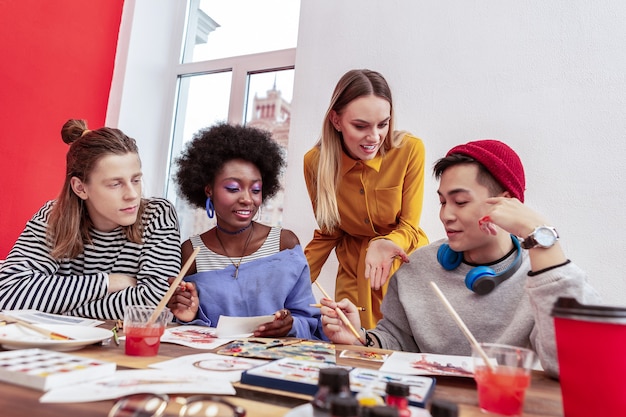 Jefe de equipo. Líder del equipo de jóvenes diseñadores de moda de pelo rubio hablando con ellos mientras trabaja