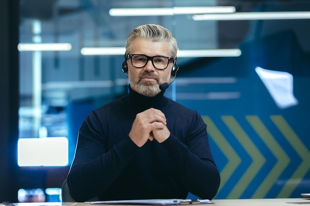 Jefe de pelo gris maduro con auriculares de videollamada escuchando una conversación en una reunión en línea